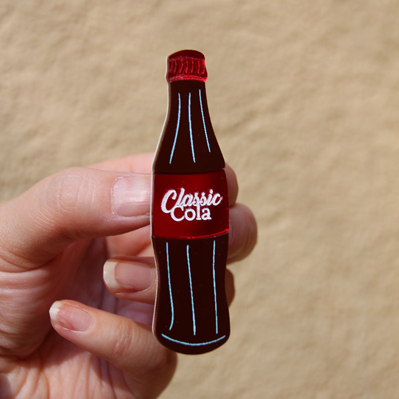 Hand holding a miniature Coca-Cola bottle against a beige background